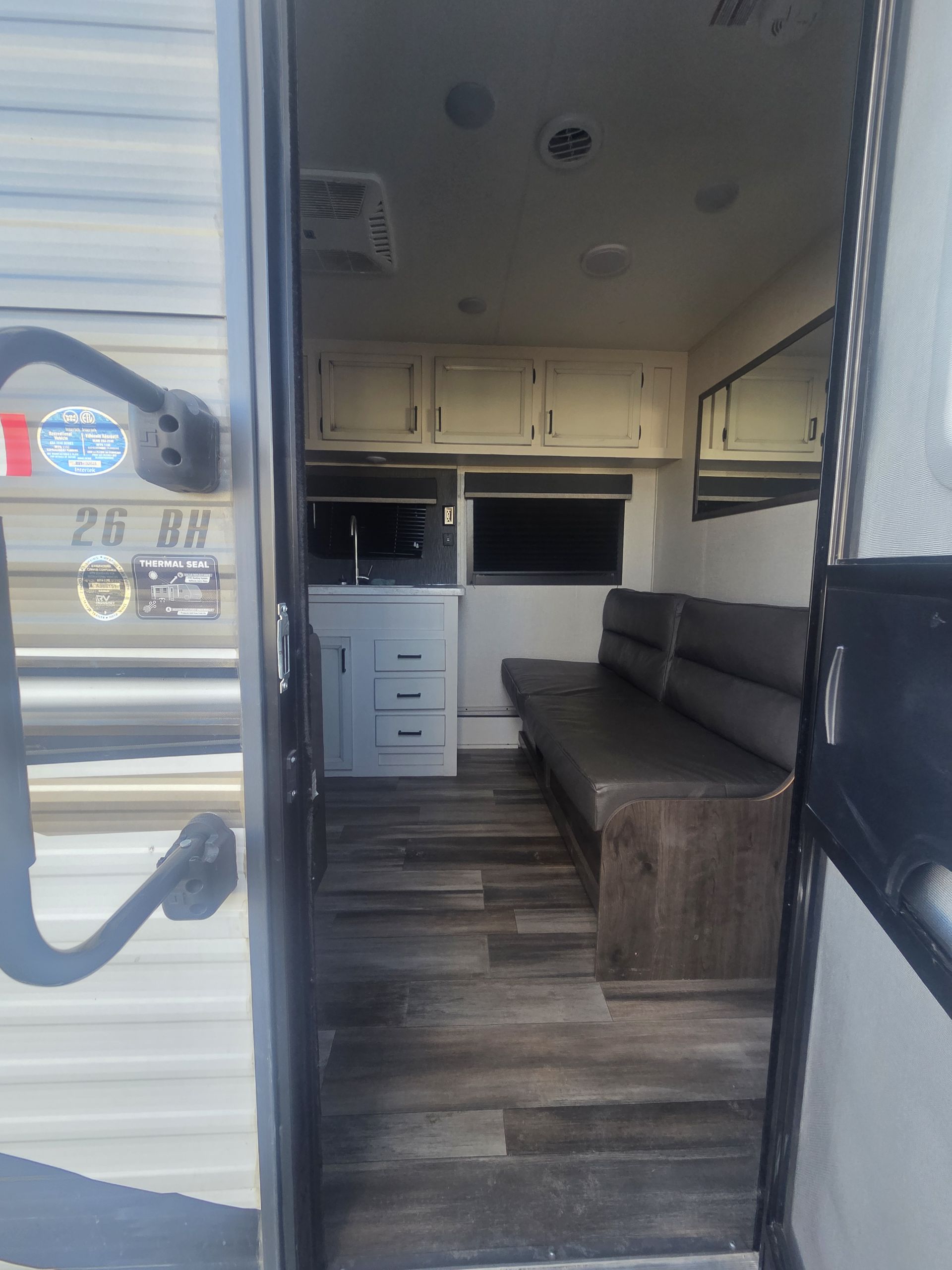 Image of the inside of a camper clicked through the front entrance. Inside the camper a sofa and some cabinets are visible.